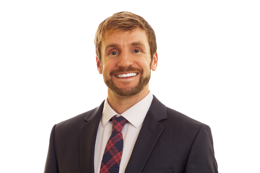 This Brian Charles Steel photo is a headshot of a salesman in a dark gray suit.  He is centered in the frame.  The lower portion of the frame contains his upper chest, and the top of his head is in the top portion of the frame.  He is wearing a white shirt with a red and blue plaid tie.  He has tan skin and blonde hair.  His hair is combed neatly to the right.  He is lit with a Rembrandt style; the right side slightly darker than the left. The background is white. 